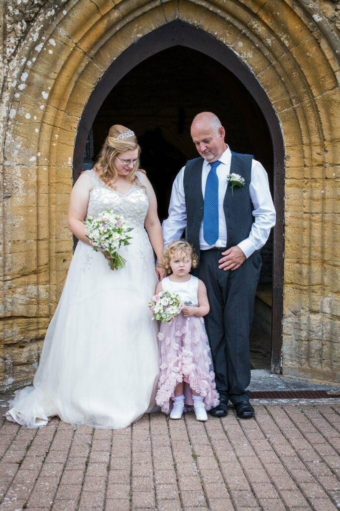 The bride and groom with their daughter at the doorway of Abbey Manor in Yeovil, Somerset.